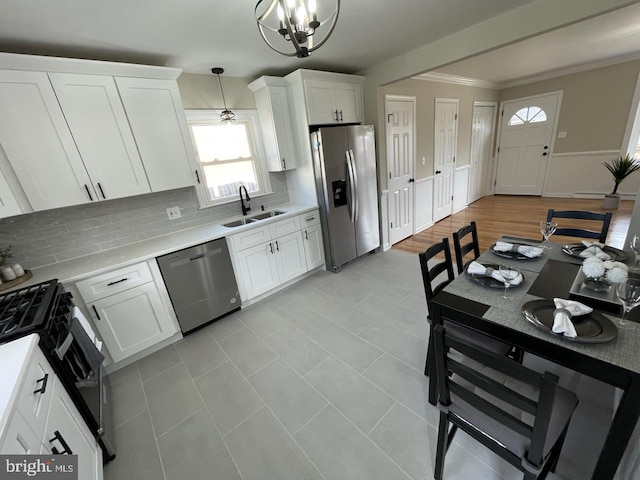 kitchen with stainless steel appliances, a sink, white cabinets, light countertops, and pendant lighting