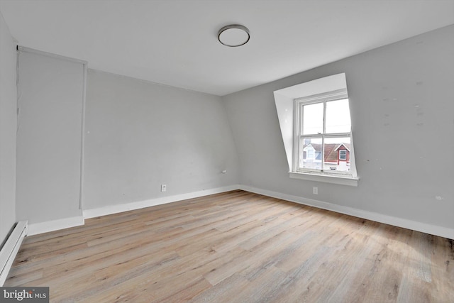 empty room featuring light wood-style floors, a baseboard radiator, and baseboards