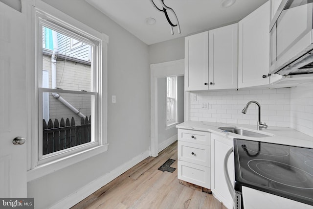 kitchen with stainless steel microwave, backsplash, electric range, white cabinetry, and a sink