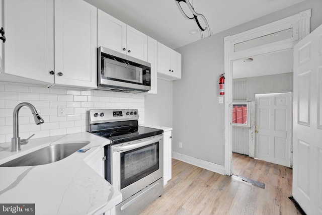 kitchen with appliances with stainless steel finishes, light stone countertops, light wood-type flooring, white cabinetry, and a sink