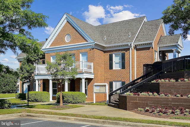 colonial house featuring brick siding, stairway, a balcony, and roof with shingles