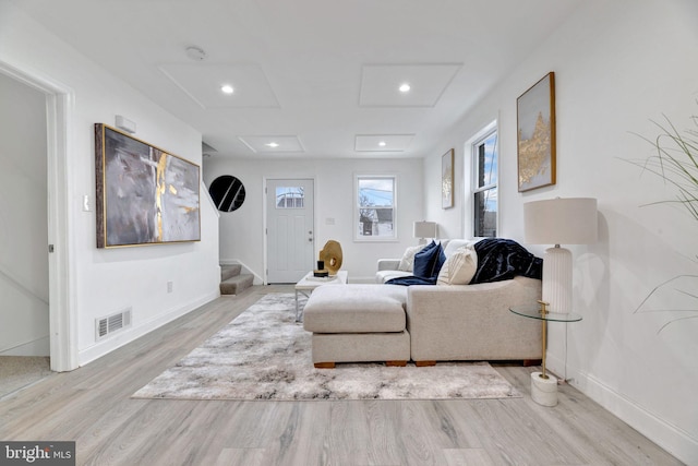 living area with attic access, visible vents, light wood-style flooring, and baseboards