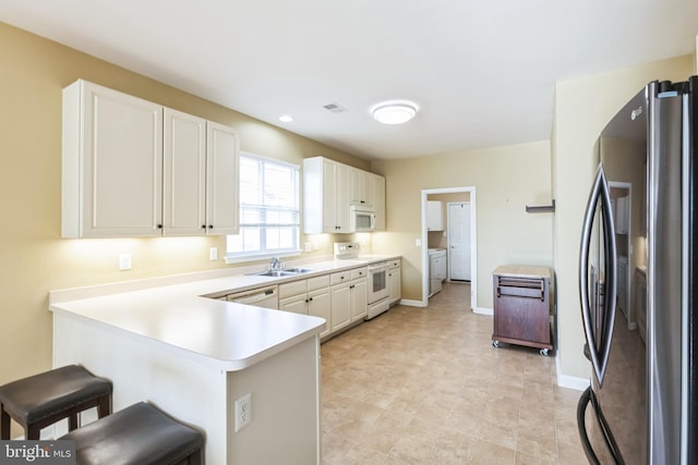 kitchen with a breakfast bar area, light countertops, white cabinetry, white appliances, and a peninsula