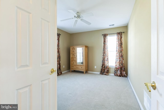 empty room featuring a ceiling fan, light colored carpet, visible vents, and baseboards