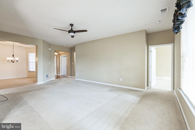 unfurnished living room with light colored carpet, visible vents, baseboards, and ceiling fan with notable chandelier