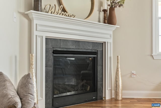 interior details with wood finished floors, a tile fireplace, and baseboards