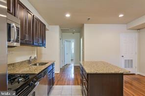 kitchen with visible vents, a center island, light stone countertops, dark brown cabinetry, and appliances with stainless steel finishes