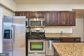 kitchen with dark brown cabinetry, light stone countertops, appliances with stainless steel finishes, and a sink