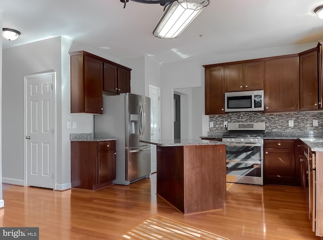 kitchen featuring light wood-type flooring, light stone countertops, appliances with stainless steel finishes, and a center island