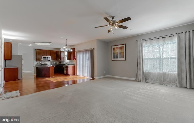 unfurnished living room featuring light colored carpet, ceiling fan, and baseboards