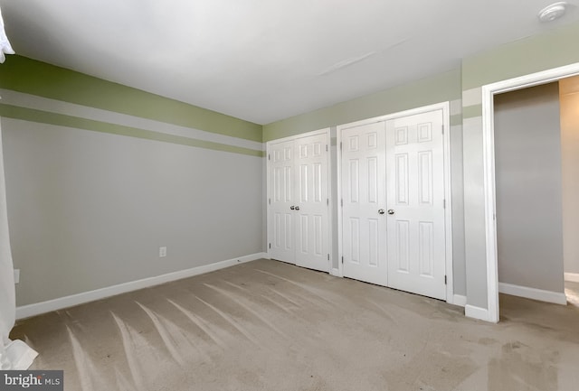 unfurnished bedroom with baseboards, multiple closets, and light colored carpet