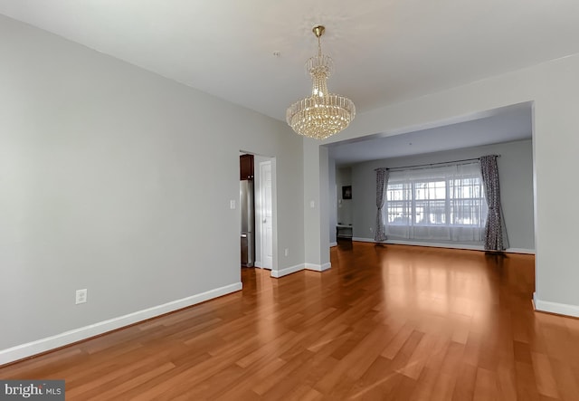 empty room featuring baseboards, a chandelier, and wood finished floors