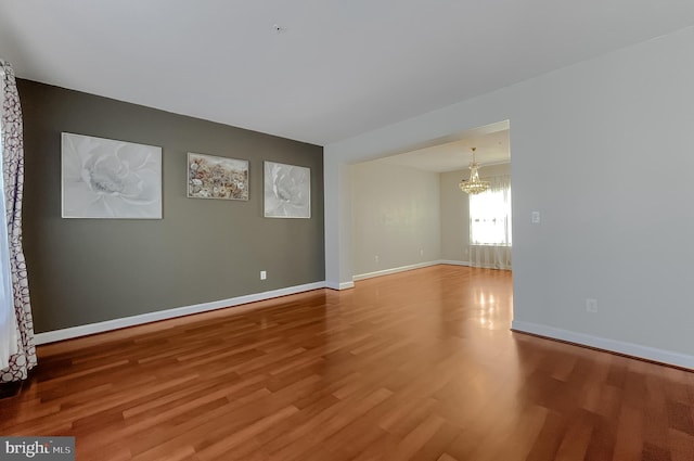 unfurnished room featuring baseboards, wood finished floors, and an inviting chandelier