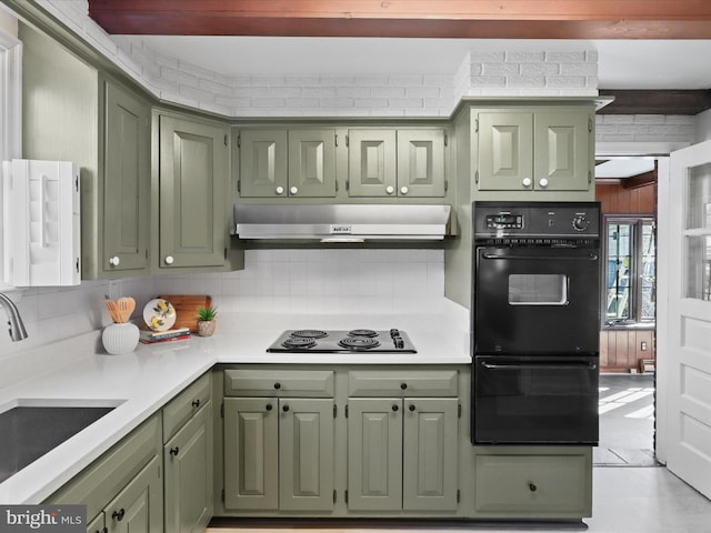 kitchen featuring green cabinetry, a sink, black appliances, under cabinet range hood, and tasteful backsplash