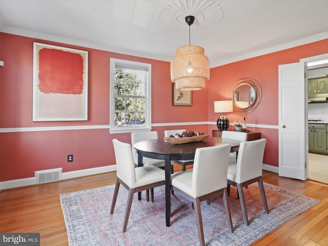 dining room featuring visible vents, crown molding, baseboards, and wood finished floors