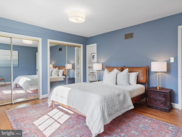 bedroom featuring visible vents, baseboards, multiple closets, and wood finished floors