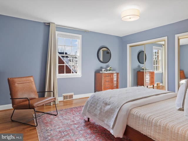 bedroom with visible vents, multiple windows, wood finished floors, and baseboards