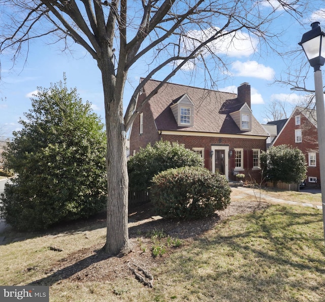 view of front facade with a front yard, brick siding, and a chimney