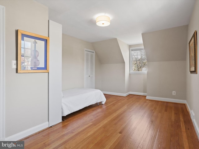 unfurnished bedroom with lofted ceiling, a closet, baseboards, and wood-type flooring