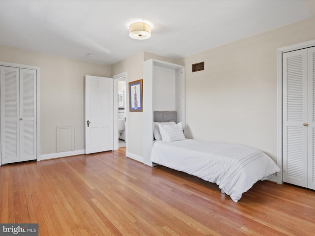 bedroom featuring visible vents, light wood-style flooring, baseboards, and multiple closets