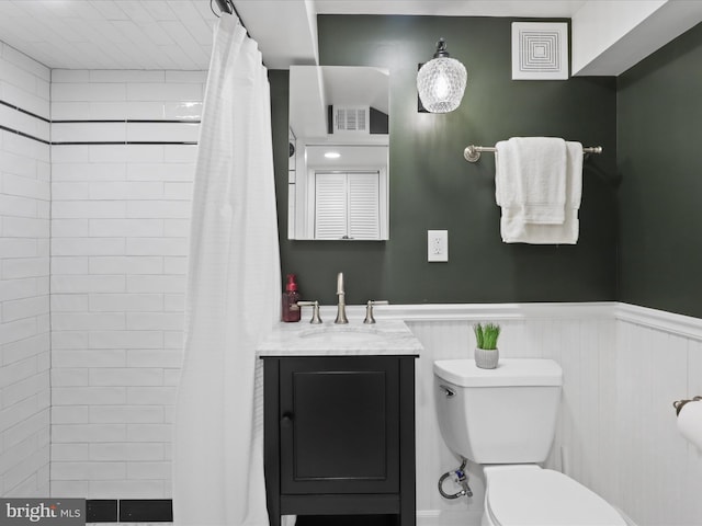 full bathroom featuring visible vents, toilet, a tile shower, wainscoting, and vanity