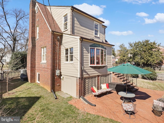 back of property with brick siding, a lawn, a chimney, and fence