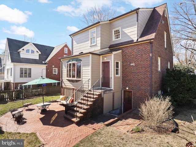 view of front facade with a patio, brick siding, and fence