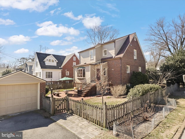 view of front of home featuring an outdoor structure, a detached garage, brick siding, and a fenced front yard