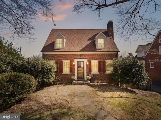 cape cod home featuring brick siding and a chimney