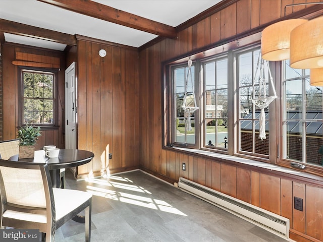 dining area with wooden walls, concrete floors, baseboards, beam ceiling, and a baseboard radiator