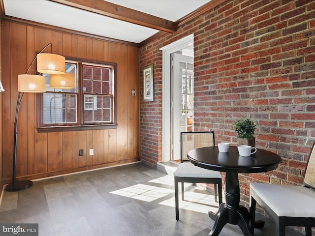 unfurnished dining area with beam ceiling, plenty of natural light, brick wall, and wooden walls