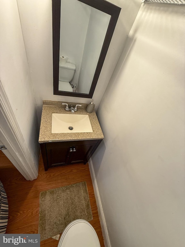 half bathroom featuring wood finished floors, vanity, toilet, and baseboards