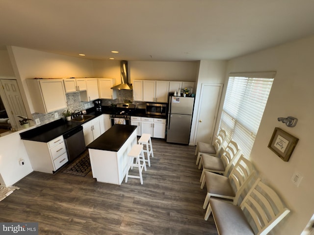 kitchen with tasteful backsplash, dark countertops, appliances with stainless steel finishes, a sink, and wall chimney range hood