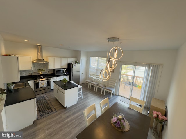 kitchen featuring white cabinets, dark countertops, a kitchen island, stainless steel appliances, and wall chimney range hood