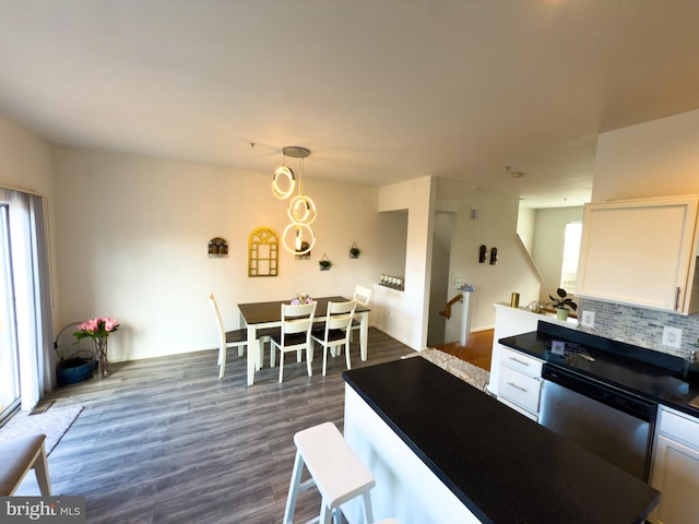 kitchen featuring dark wood-type flooring, white cabinetry, stainless steel dishwasher, decorative backsplash, and dark countertops