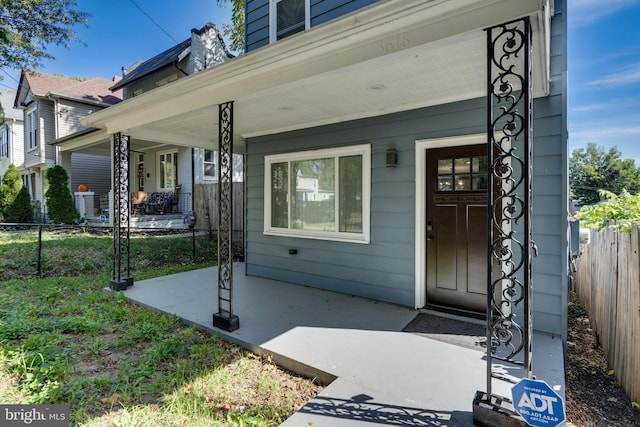 view of exterior entry with covered porch and fence