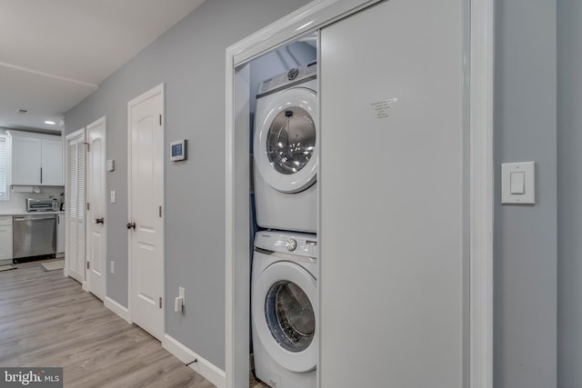 clothes washing area with a toaster, stacked washer / drying machine, light wood-style flooring, laundry area, and baseboards