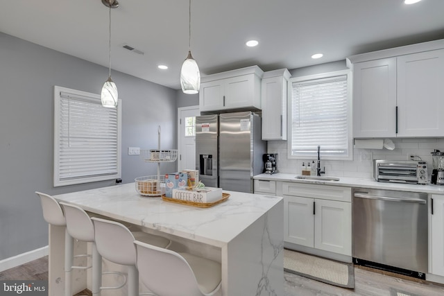 kitchen with pendant lighting, stainless steel appliances, white cabinets, a sink, and a kitchen island