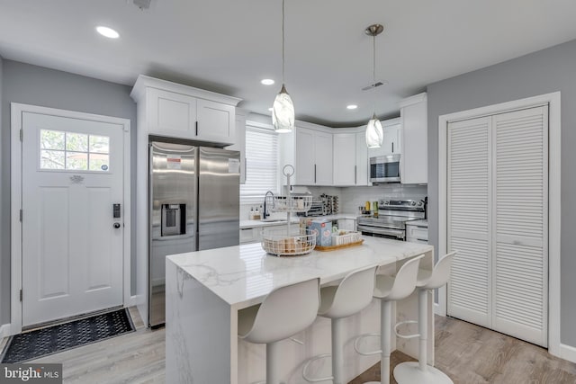 kitchen with decorative light fixtures, stainless steel appliances, white cabinets, a kitchen island, and light stone countertops