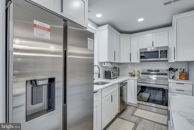 kitchen featuring white cabinets, light stone counters, stainless steel appliances, and backsplash