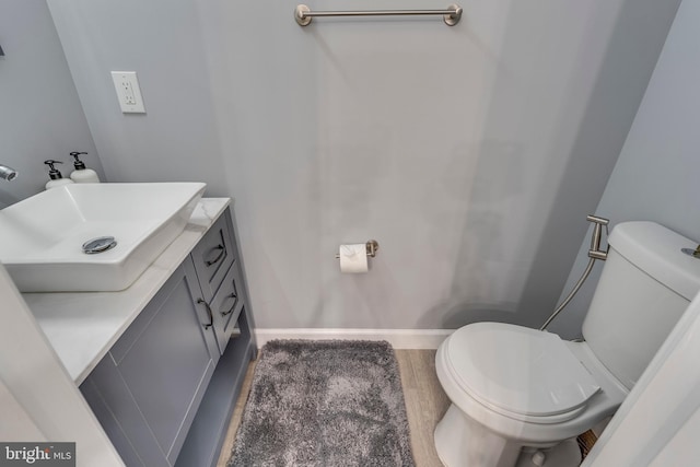 half bathroom with toilet, vanity, baseboards, and wood finished floors