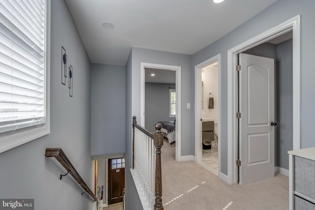 hall with baseboards, an upstairs landing, and light colored carpet