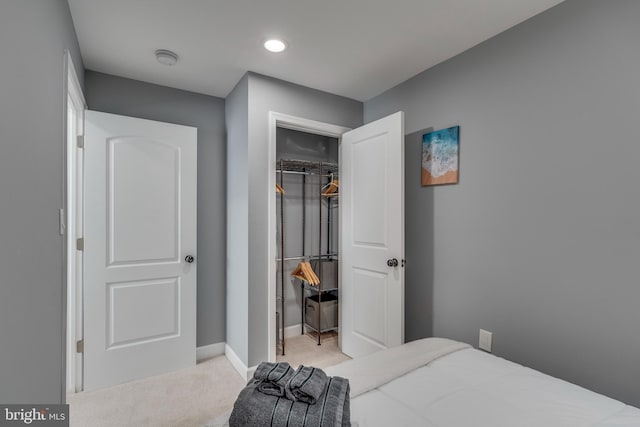 bedroom featuring light carpet, a spacious closet, a closet, and baseboards