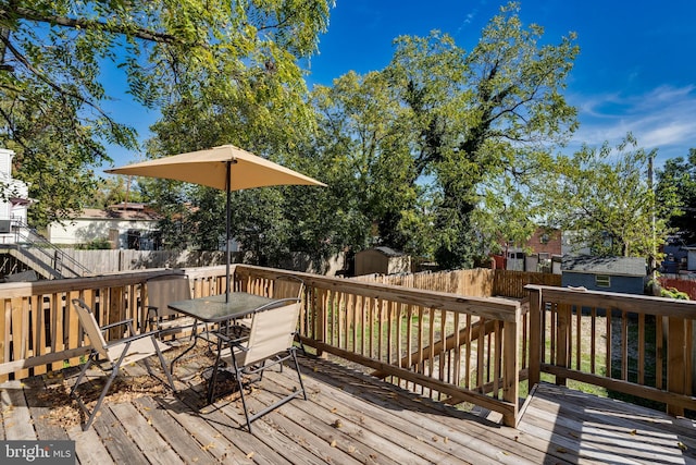 wooden terrace featuring a storage shed, a fenced backyard, outdoor dining area, and an outbuilding