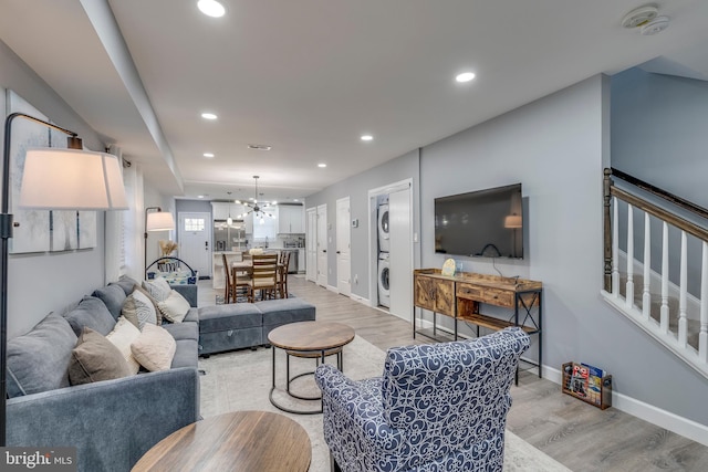 living area with a chandelier, light wood finished floors, stacked washer and clothes dryer, and recessed lighting