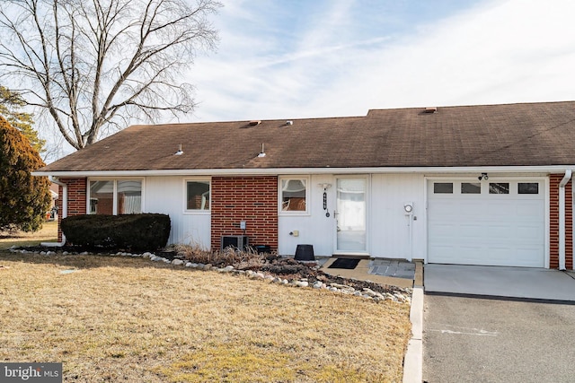 ranch-style house featuring brick siding, concrete driveway, roof with shingles, an attached garage, and a front yard