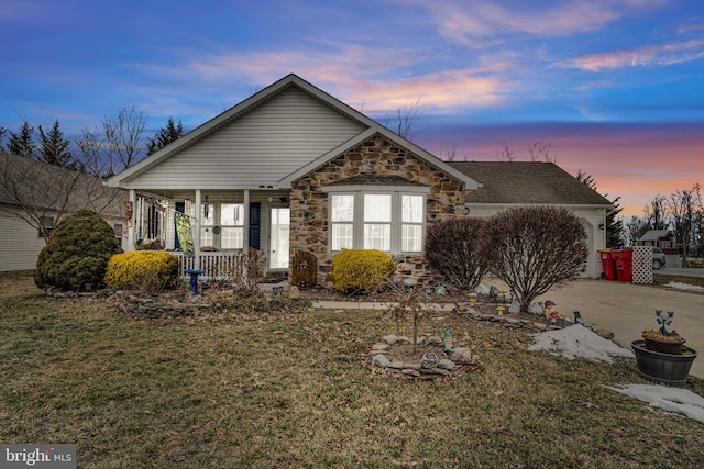 view of front of house featuring covered porch, a garage, stone siding, driveway, and a front lawn