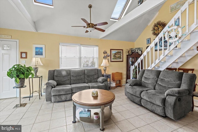 living room with a skylight, light tile patterned floors, ceiling fan, stairway, and high vaulted ceiling