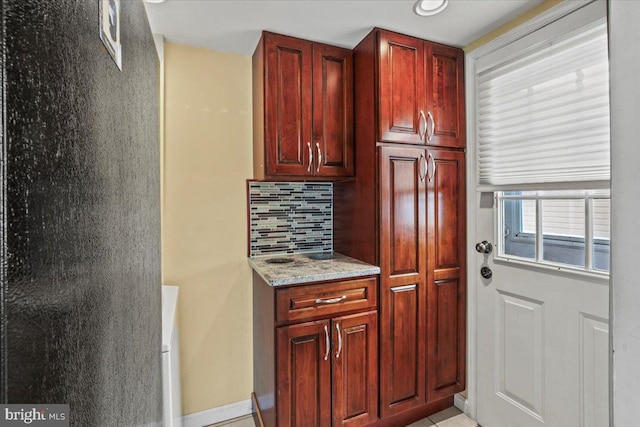 kitchen featuring dark brown cabinets, light stone countertops, and decorative backsplash