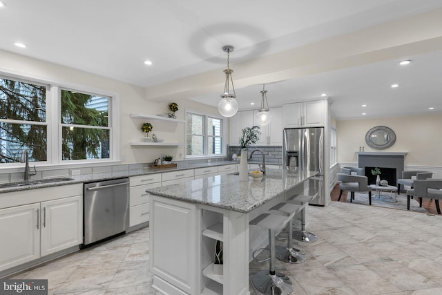 kitchen with a fireplace, open shelves, stainless steel appliances, white cabinetry, and a sink